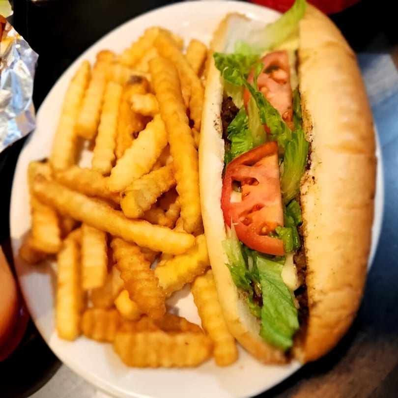 A DaBomb Sports Grill cheesesteak with lettuce and tomato, served with a side of crinkle-cut fries.
