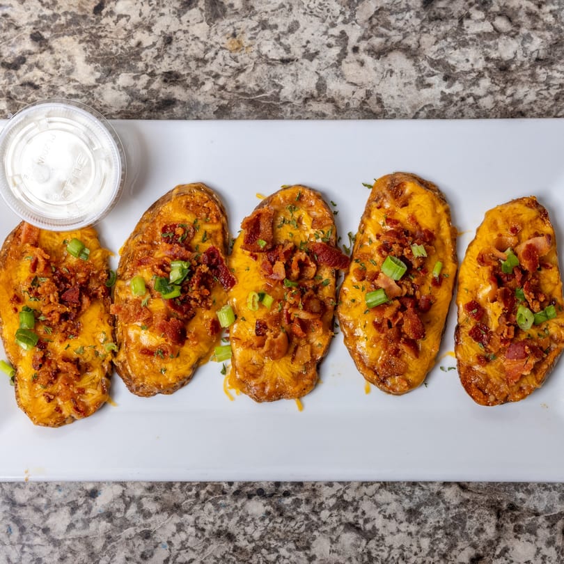 Five potato skins topped with melted cheese, bacon bits, and green onions, with a side of sour cream.