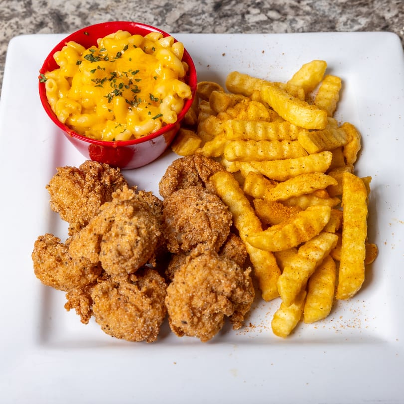 A plate of fried chicken nuggets, crinkle-cut fries, and a red bowl of mac and cheese.